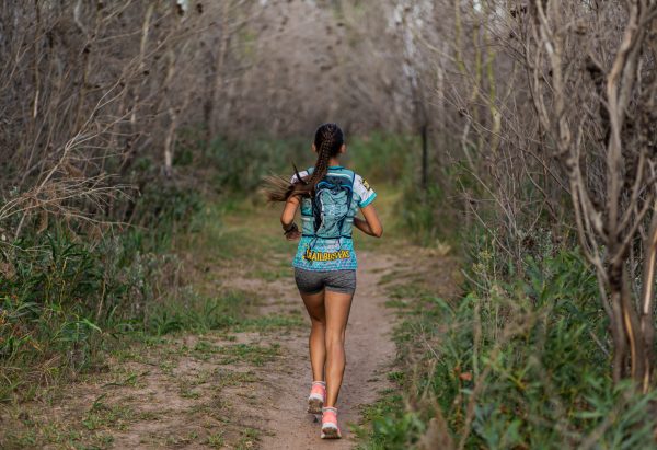 Photo of women running on a trail wearing a Trailbusters shirt.